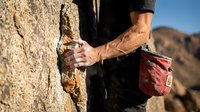 Close-up of male rock climber's hands gripping textured sandstone cliff face during outdoor adventure climbing session in desert mountain landscape.