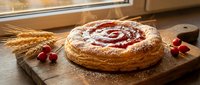 Homemade cherry puff pastry tart with powdered sugar on wooden board, fresh berries and wheat stalks for rustic bakery dessert presentation.