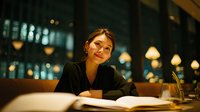 Young professional woman working late at night in modern office with city lights background, business lifestyle and career dedication concept.