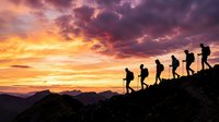 Silhouetted hikers ascending mountain ridge at sunset, dramatic golden and purple sky, teamwork and progression concept for motivational and outdoor adventure projects.