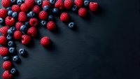 Fresh mixed berries raspberries and blueberries scattered on dark wooden background with copy space for healthy eating and nutrition concepts.
