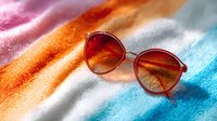Round red sunglasses with gradient lenses on colorful orange, pink and blue textured background with soft shadows and sunlight effect for summer fashion concept.
