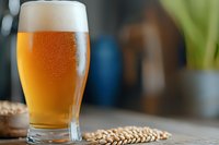 Fresh cold craft beer in glass with foam head and wheat ears on wooden table, blurred background with bokeh lights and copy space.