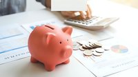 Pink piggy bank with coins and calculator on financial documents for savings and budget planning concepts.