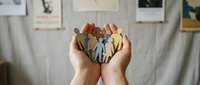 Hands holding colorful wooden family figures representing unity, care and togetherness in home environment with gallery wall background.