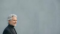 Mature man with gray hair wearing black turtleneck, smiling in profile against neutral gray background for corporate and lifestyle use.