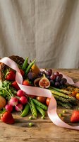 Fresh seasonal produce basket with strawberries, figs, grapes, asparagus, peas and pink ribbon on rustic wooden table for healthy eating and cooking.