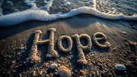 Word hope written in sand on beach with gentle wave approaching, seashells scattered nearby, sunlight creating warm glow on wet sand surface.