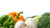 Fresh organic vegetables including broccoli, bell peppers, mushrooms and onions arranged on white background for healthy cooking and nutrition concepts.