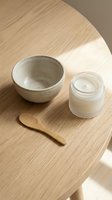 Overhead view of skincare and beauty products arranged on light wood surface with ceramic bowl, cream jar, and wooden applicator for cosmetics, spa, wellness, and natural beauty routines.