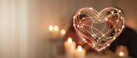 Glowing heart-shaped light trails created with long exposure photography against warm candlelit background for romantic occasions and love concepts.