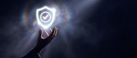 Hand holding a glowing shield with checkmark icon on dark background, symbolizing cybersecurity, data protection, and digital safety.