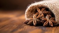 Star anise pods spilling from burlap sack onto rustic wooden surface in warm lighting, creating aromatic cooking and baking composition with natural textures.