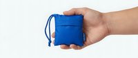 Compact blue foldable bag held in hand, showing its small packable size. Reusable eco-friendly tote packed into a tiny pouch for travel and shopping.