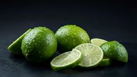 Fresh green limes whole and sliced on dark background for culinary cooking ingredients and citrus fruit recipes in kitchen food photography.
