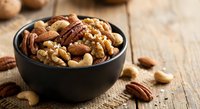 Mixed nuts and seeds in black bowl on rustic wooden table for healthy snacking and cooking ingredients.