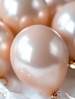 Soft peach-colored party balloons with delicate sheen create dreamy celebratory atmosphere, featuring close-up of single balloon with gentle bokeh effect in background.