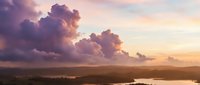 Dramatic sunset sky with purple and pink clouds over serene landscape with water reflections creating peaceful evening atmosphere for nature backgrounds.