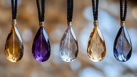 Colorful crystal pendants on black cords hanging in row - amber, purple, clear, golden and blue teardrop gemstones with metallic caps for jewelry making.