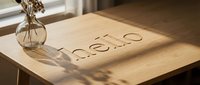 Hello word carved into a light wooden table surface with natural sunlight and shadows, glass vase with dried flowers, warm cozy interior.