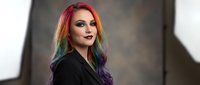 Young woman with vibrant rainbow colored hair and dark makeup wearing black blazer in professional portrait style for business and fashion concepts.