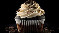 Chocolate cupcake with swirled vanilla buttercream frosting topped with chocolate sprinkles on dark background with scattered cocoa crumbs, macro food photography.