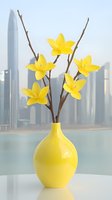Yellow ceramic vase with artificial daffodils against modern city skyline background. Minimalist spring decor arrangement on white surface creates serene urban atmosphere.
