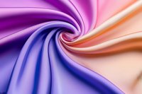Smooth gradient silk fabric swirled in spiral pattern featuring purple, blue, and peach colors with soft luxurious texture and flowing curves creating dynamic movement.