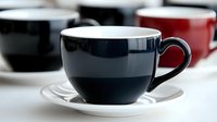 Dark navy coffee cup and white saucer arrangement with blurred cups in background creating minimalist composition for cafe and restaurant marketing.