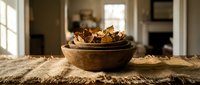 Rustic wooden bowl filled with dried autumn leaves on burlap fabric in cozy farmhouse kitchen interior with warm natural lighting for home decor projects.