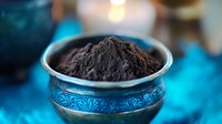 Dark cocoa powder in ornate turquoise metallic bowl against blue background with soft bokeh lighting, raw ingredient for chocolate making and baking.
