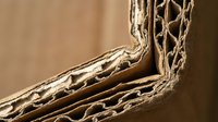 Corrugated cardboard edge showing detailed fluted structure and layers in warm brown tones for packaging and shipping industry applications.