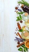 Essential oils in glass bottles with fresh herbs, spices and dried orange slices arranged on white wooden background for aromatherapy and natural wellness.