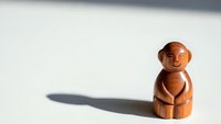 Wooden carved monkey figurine sitting peacefully on white surface with soft shadow, handcrafted artisan sculpture for meditation and zen decor.