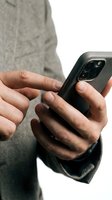Man with medium skin tone wearing gray casual clothing holding black smartphone with dual camera setup, isolated on white background for app design and mobile technology concepts.