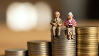 Senior couple miniature figures sitting on stacked coins representing retirement planning, pension savings, financial security and investment growth.