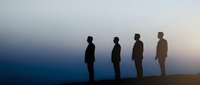 Four business professionals standing in silhouette against dramatic twilight sky, representing teamwork, leadership and corporate success concepts.