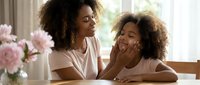 Mother and daughter with curly hair sharing joyful moment together at home, laughing and bonding indoors near window with flowers.