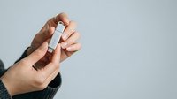 Close-up of male hand holding white rectangular product box against neutral background for packaging mockup and branding purposes.