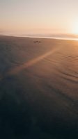Solitary figure lying on vast sandy beach at golden hour sunrise or sunset, with rippled wet sand texture and calm ocean horizon in warm amber light, suitable for wellness, meditation, and lifestyle concepts.