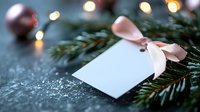 Blank gift tag with pink silk bow on pine branches against dark background with bokeh lights and Christmas ornaments, festive holiday composition.