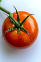 Fresh ripe red tomato with green stem and water droplets on smooth surface, macro photography showing detailed texture and natural organic produce.
