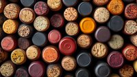 Wine corks collection arranged in rows showing variety of colors and textures from red wine and white wine bottles, natural and synthetic materials.