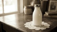 Fresh milk bottle on vintage lace doily in rustic kitchen setting with warm natural lighting and wooden table surface for dairy product advertising.