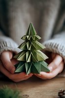 Green origami Christmas tree held in hands against cozy sweater background, perfect for holiday crafting and sustainable decoration ideas.