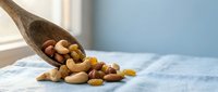 Mixed nuts and dried fruits spilling from wooden spoon on kitchen counter. Healthy snacking and cooking ingredients for nutritious meals and recipes.