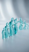 Translucent turquoise glass figurines arranged in group formation on reflective surface with soft lighting for business teamwork and leadership concepts.