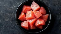 Fresh raw salmon cubes in black ceramic bowl on dark concrete background. Clean eating and healthy omega-3 rich seafood for cooking.