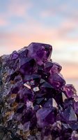 Amethyst crystal cluster glowing with deep violet hues against a soft pastel sunset sky, showcasing natural gemstone texture and sparkle.