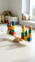 Colorful wooden building blocks balanced on seesaw in bright playroom with toys and books creating educational learning environment for children development.
